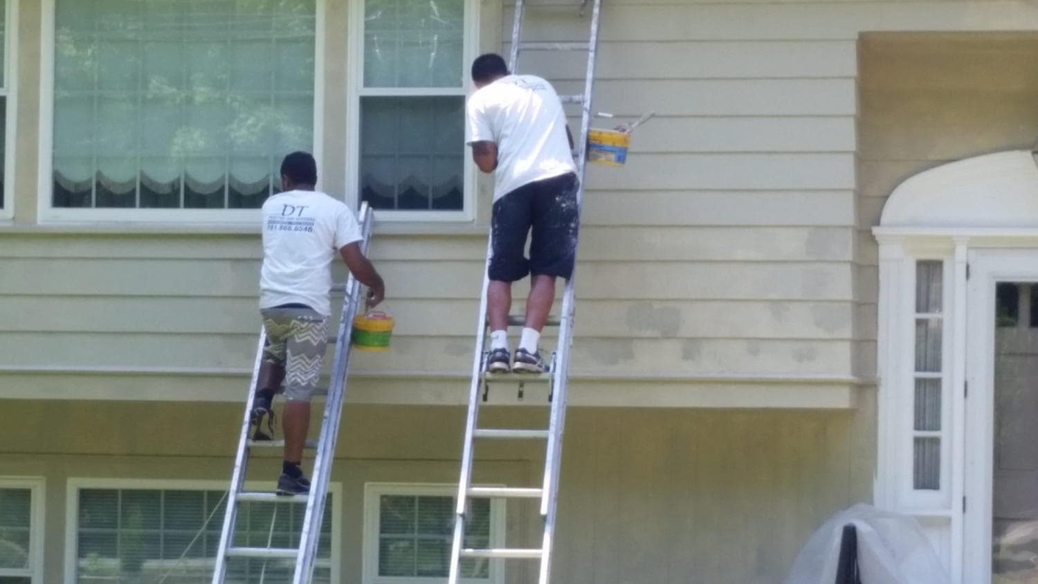 Two DT painters on ladders repainting the siding of a house