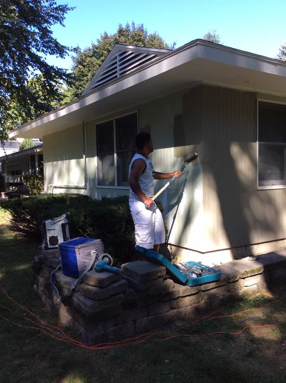 Painter working on the siding of a ranch house