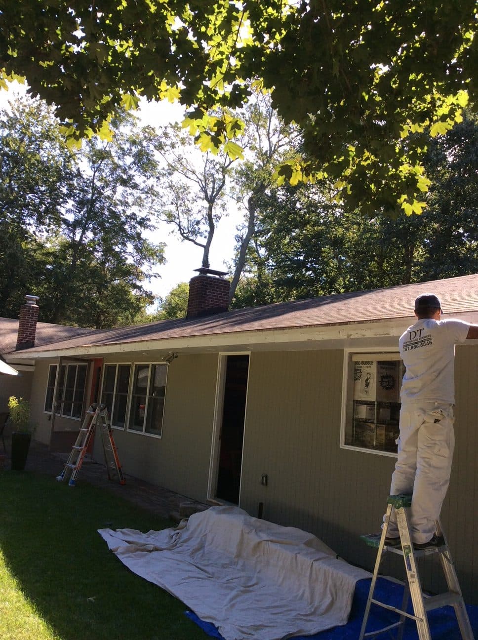Painter on a ladder at a ranch house with drop cloths spread on the lawn