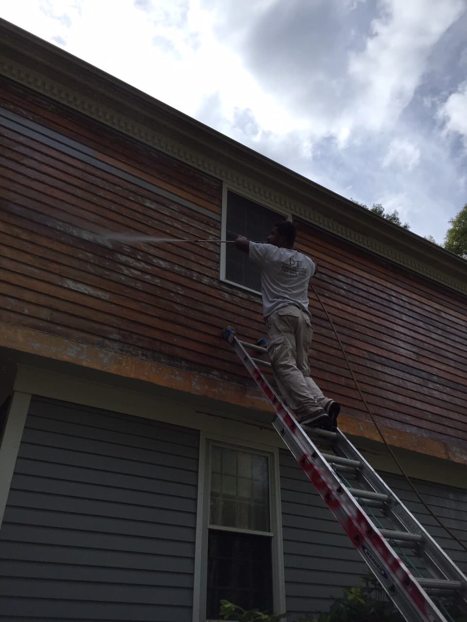 Painter on a tall ladder painting a second-story wall
